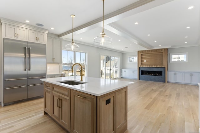 kitchen featuring a sink, light wood finished floors, a large fireplace, built in refrigerator, and ornamental molding