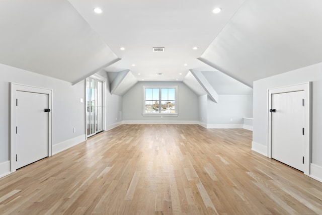 additional living space with baseboards, visible vents, vaulted ceiling, and light wood-type flooring