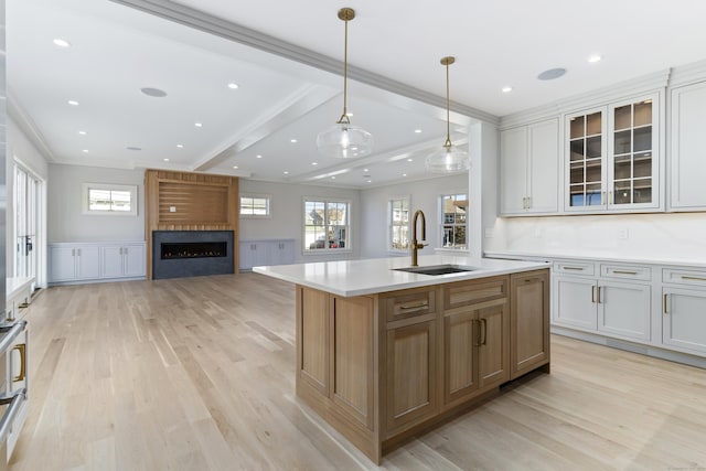 kitchen with a sink, a large fireplace, ornamental molding, and light wood-type flooring