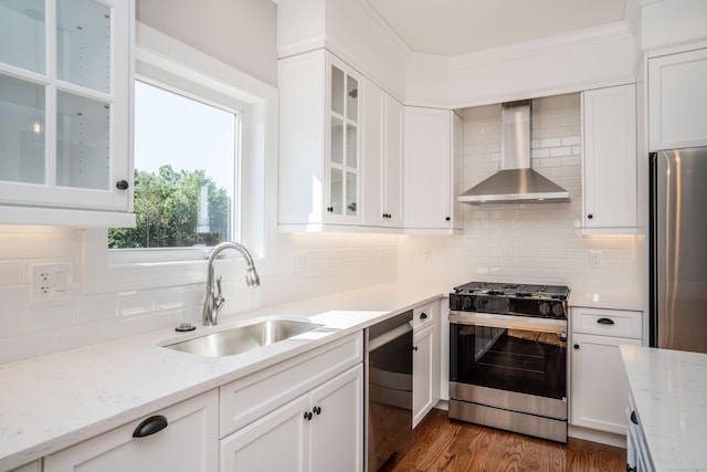 kitchen featuring sink, appliances with stainless steel finishes, white cabinets, wall chimney range hood, and backsplash