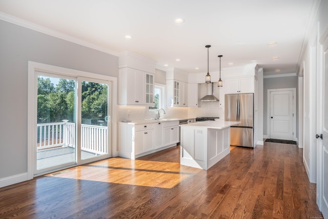 kitchen featuring pendant lighting, wall chimney range hood, stainless steel refrigerator, a center island, and white cabinets