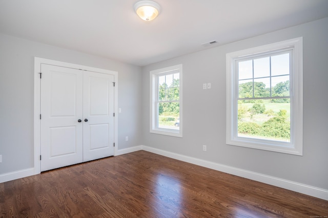 unfurnished bedroom featuring multiple windows, a closet, and dark hardwood / wood-style floors