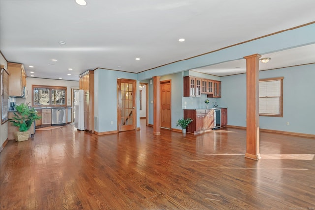 unfurnished living room with ornate columns, beverage cooler, dark wood-style floors, and baseboards