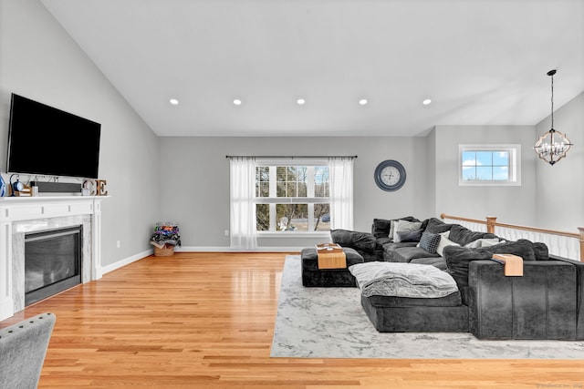 living room featuring an inviting chandelier, lofted ceiling, a high end fireplace, and light wood-type flooring