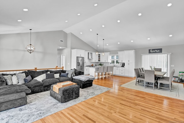 living room with a chandelier, high vaulted ceiling, and light hardwood / wood-style flooring