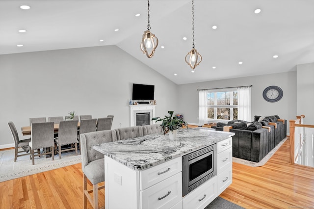 kitchen with white cabinetry, light wood-type flooring, stainless steel microwave, a kitchen island, and light stone countertops