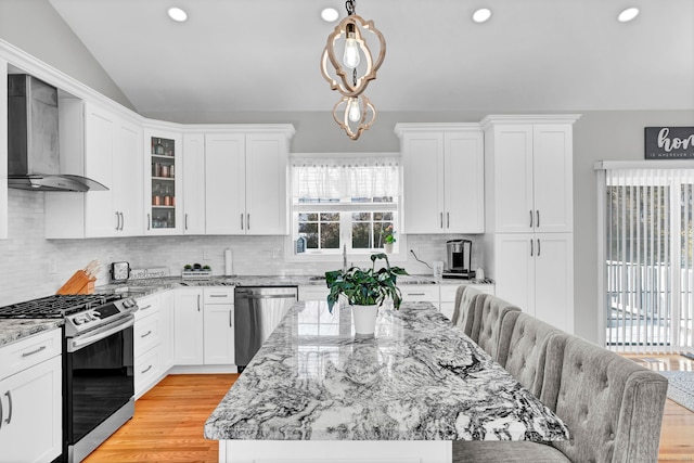 kitchen featuring pendant lighting, wall chimney range hood, appliances with stainless steel finishes, tasteful backsplash, and vaulted ceiling