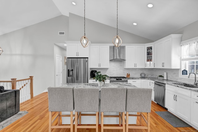 kitchen featuring wall chimney exhaust hood, sink, tasteful backsplash, a center island, and appliances with stainless steel finishes