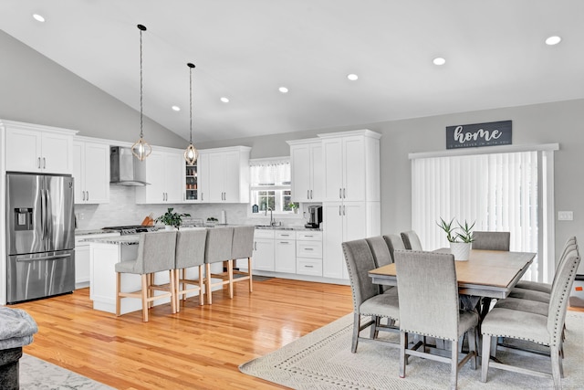 dining space with high vaulted ceiling, sink, and light hardwood / wood-style flooring