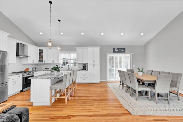 kitchen featuring pendant lighting, wall chimney range hood, appliances with stainless steel finishes, a center island, and light stone counters