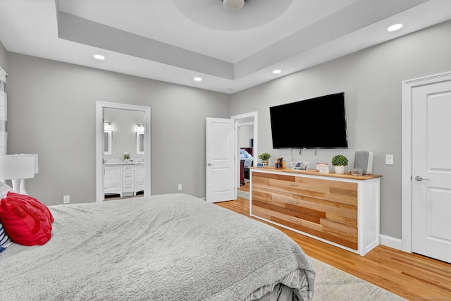 bedroom featuring connected bathroom, a tray ceiling, wood-type flooring, and ceiling fan