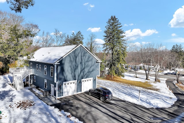 view of snow covered exterior featuring a garage, a wooden deck, and central air condition unit