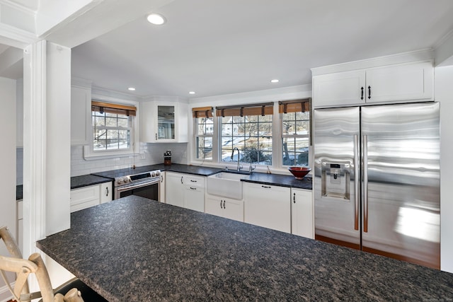 kitchen with sink, appliances with stainless steel finishes, white cabinets, dark stone counters, and backsplash