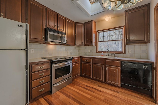 kitchen with sink, appliances with stainless steel finishes, a skylight, tasteful backsplash, and light wood-type flooring