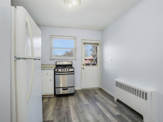 kitchen with dark wood-type flooring, stainless steel gas range oven, radiator heating unit, white fridge, and white cabinets