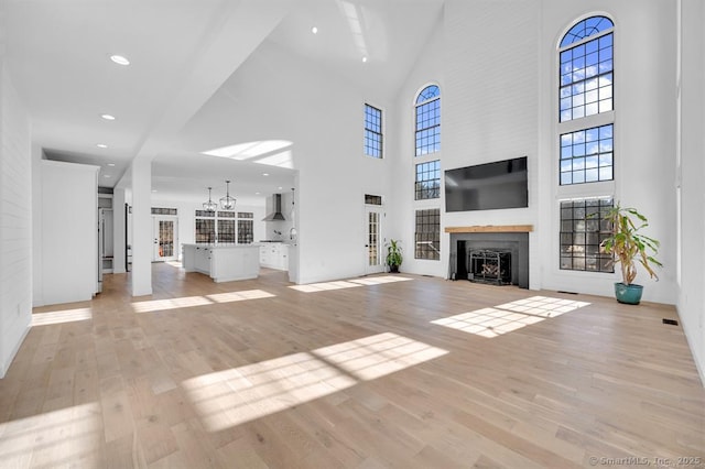 unfurnished living room with a towering ceiling, a large fireplace, and light wood-type flooring