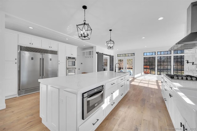 kitchen featuring white cabinetry, decorative light fixtures, stainless steel appliances, a large island, and wall chimney range hood