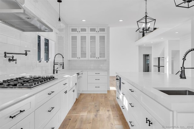 kitchen featuring wall chimney range hood, decorative light fixtures, sink, and white cabinets