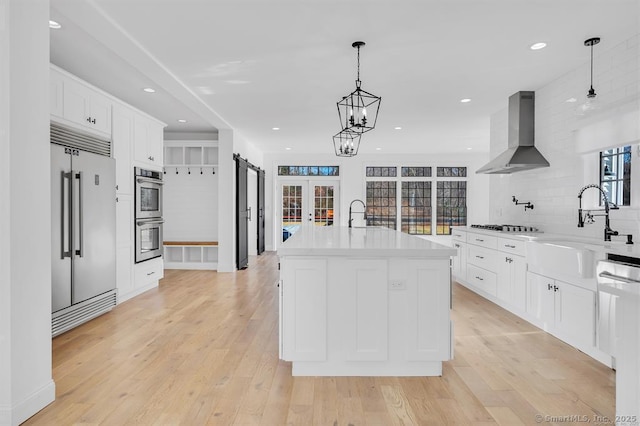 kitchen with extractor fan, appliances with stainless steel finishes, an island with sink, sink, and white cabinets