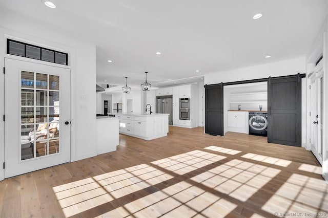 unfurnished living room featuring sink, a barn door, washer / clothes dryer, and light wood-type flooring