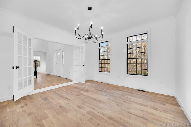 unfurnished dining area featuring a notable chandelier, crown molding, french doors, and light wood-type flooring