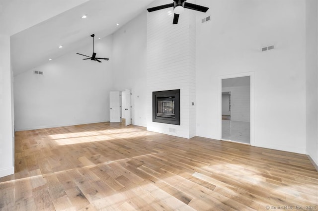 unfurnished living room featuring ceiling fan, a large fireplace, high vaulted ceiling, and light wood-type flooring