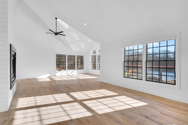 unfurnished living room featuring ceiling fan, a fireplace, light hardwood / wood-style floors, and high vaulted ceiling