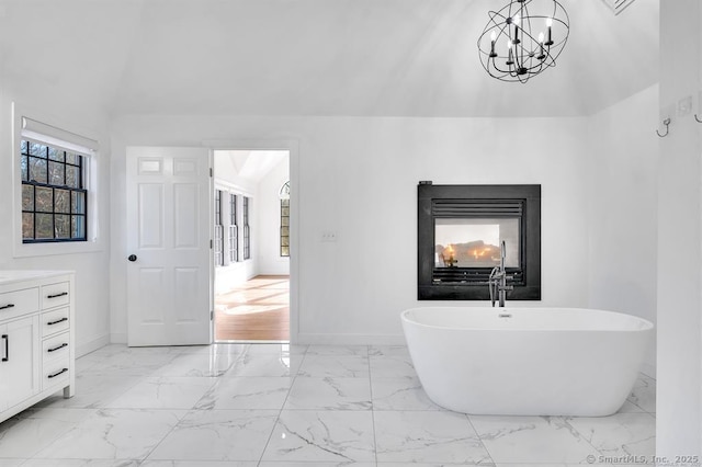 bathroom with a bathing tub, a multi sided fireplace, lofted ceiling, a chandelier, and vanity