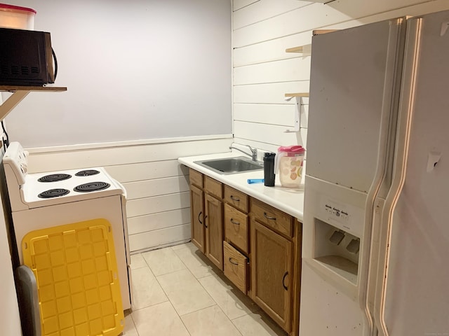 kitchen with sink, white appliances, light tile patterned floors, and wood walls