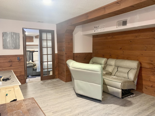 living area with wooden walls, french doors, and light wood-type flooring