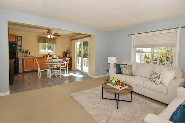 living area with light colored carpet, a textured ceiling, baseboards, and light tile patterned floors