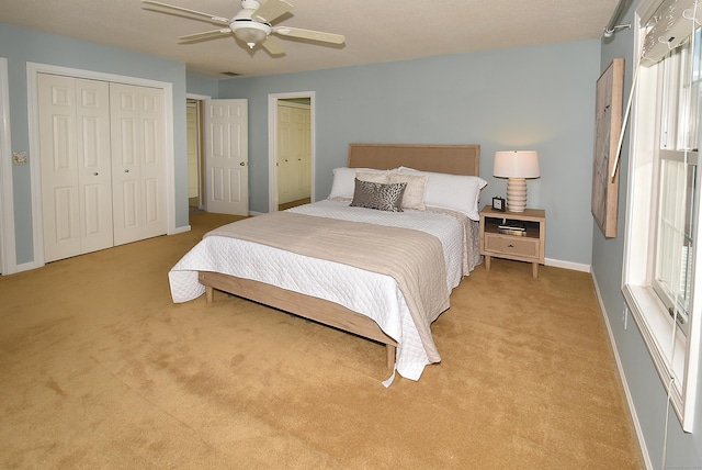 bedroom featuring two closets, light colored carpet, visible vents, ceiling fan, and baseboards