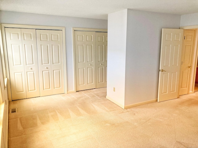 unfurnished bedroom with two closets and light colored carpet