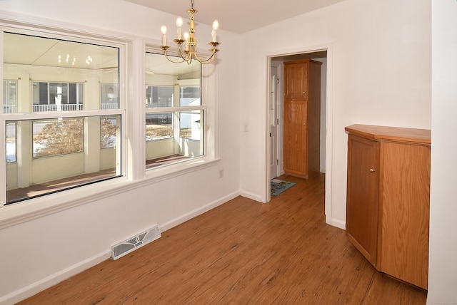 unfurnished dining area with wood-type flooring and a notable chandelier