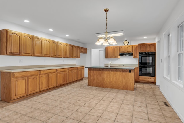 kitchen featuring black double oven, a chandelier, an island with sink, and hanging light fixtures