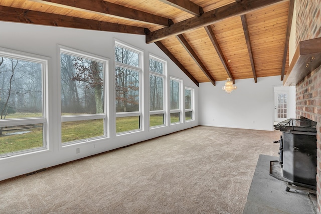 unfurnished living room featuring beam ceiling, a wealth of natural light, carpet floors, and a wood stove