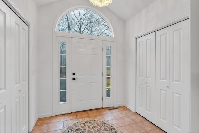 tiled foyer entrance featuring lofted ceiling, a notable chandelier, and a healthy amount of sunlight