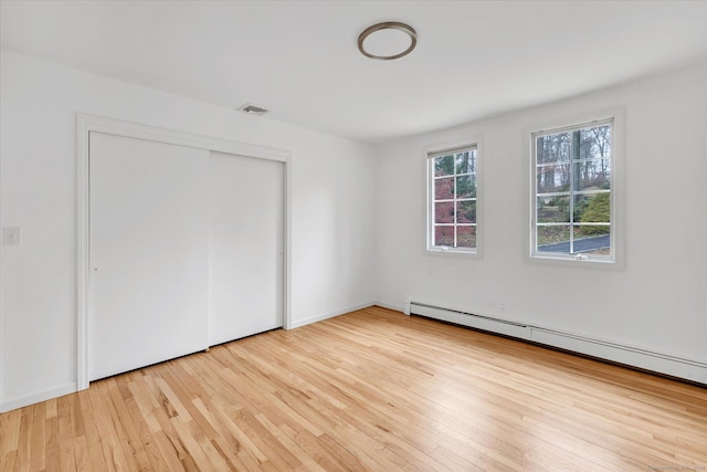 unfurnished bedroom with a baseboard radiator, light wood-type flooring, and a closet