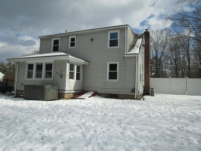 snow covered rear of property with a hot tub