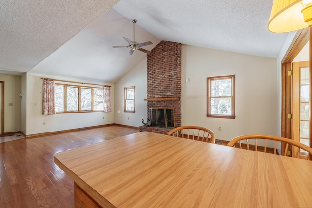 unfurnished dining area with a brick fireplace, vaulted ceiling, hardwood / wood-style floors, and a textured ceiling