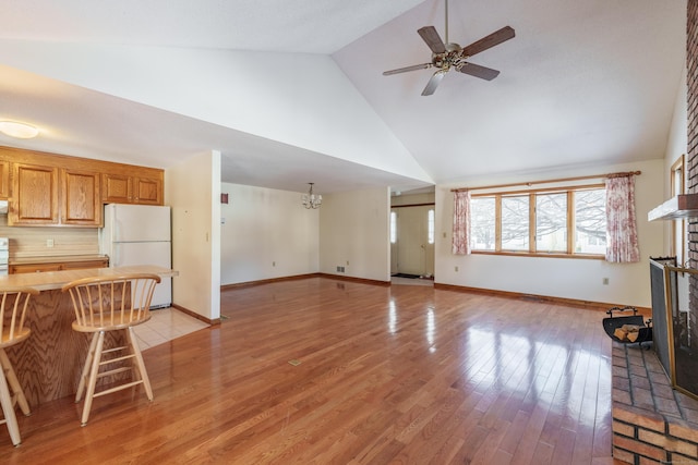 living room with ceiling fan with notable chandelier, high vaulted ceiling, light hardwood / wood-style floors, and a brick fireplace