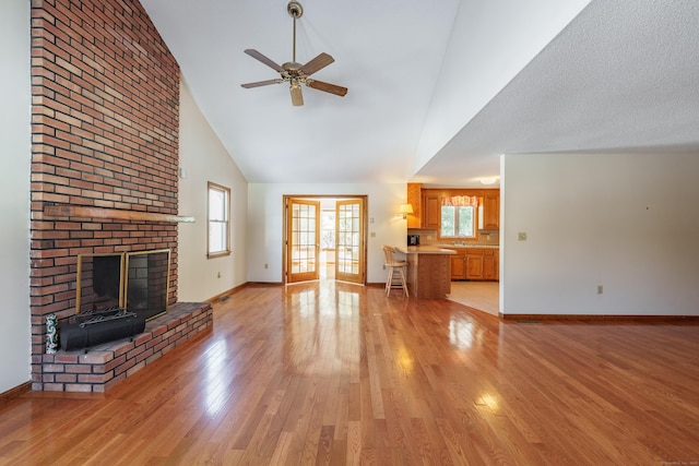 unfurnished living room with sink, high vaulted ceiling, a brick fireplace, light hardwood / wood-style flooring, and ceiling fan