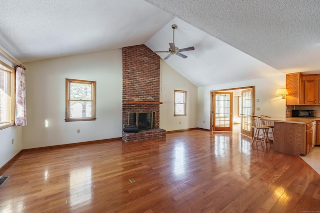 unfurnished living room with ceiling fan, plenty of natural light, a brick fireplace, and light wood-type flooring