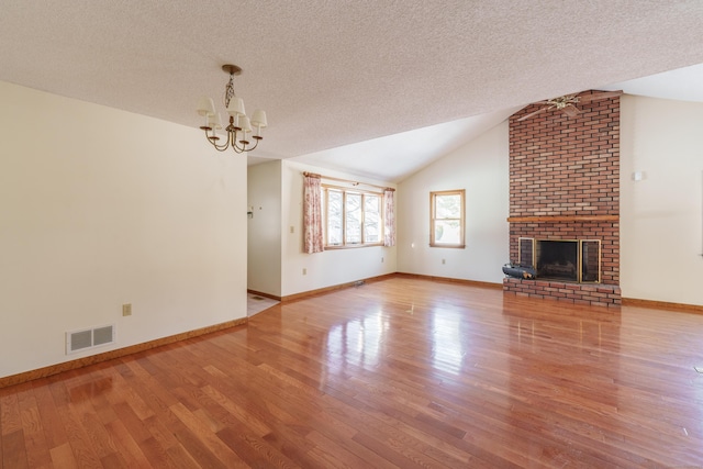 unfurnished living room with light hardwood / wood-style flooring, a textured ceiling, a brick fireplace, vaulted ceiling, and a chandelier