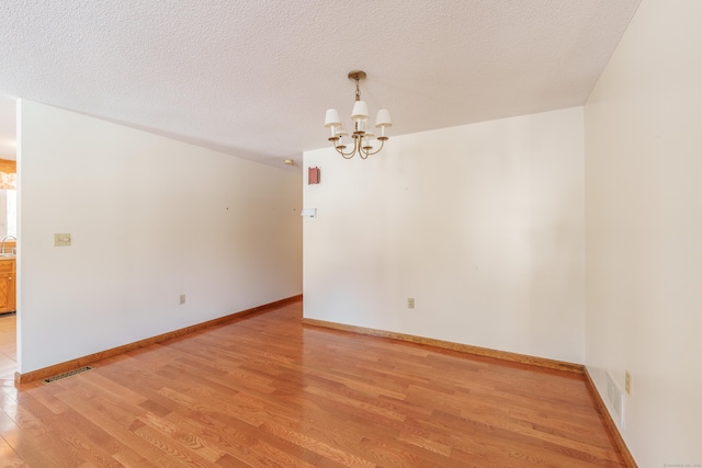 empty room featuring a chandelier, light hardwood / wood-style floors, and a textured ceiling