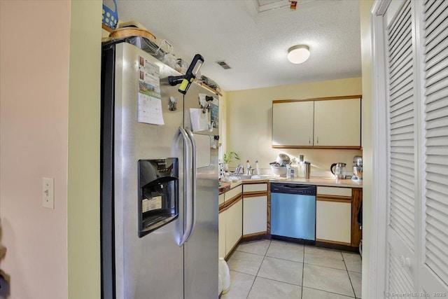 kitchen with stainless steel appliances, light tile patterned floors, a textured ceiling, and cream cabinetry