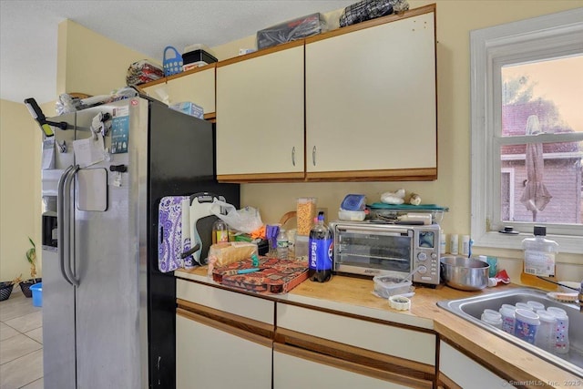 kitchen with light tile patterned flooring, sink, a textured ceiling, stainless steel fridge, and white cabinets