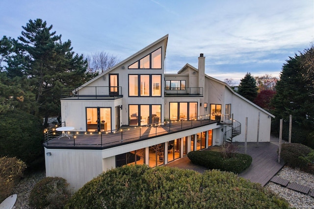 back house at dusk with a wooden deck, a patio area, and a balcony