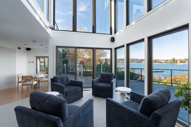 living room with a high ceiling, wood-type flooring, a water view, and a healthy amount of sunlight