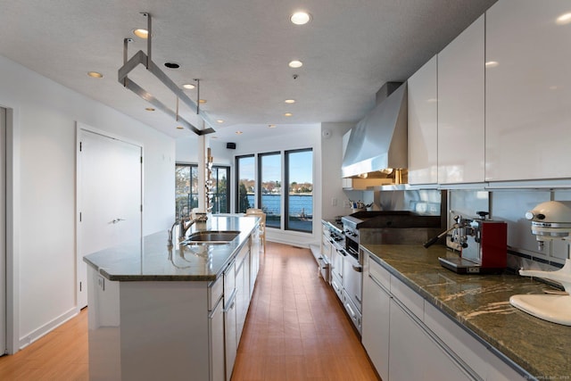 kitchen featuring extractor fan, sink, white cabinets, a kitchen island with sink, and light wood-type flooring